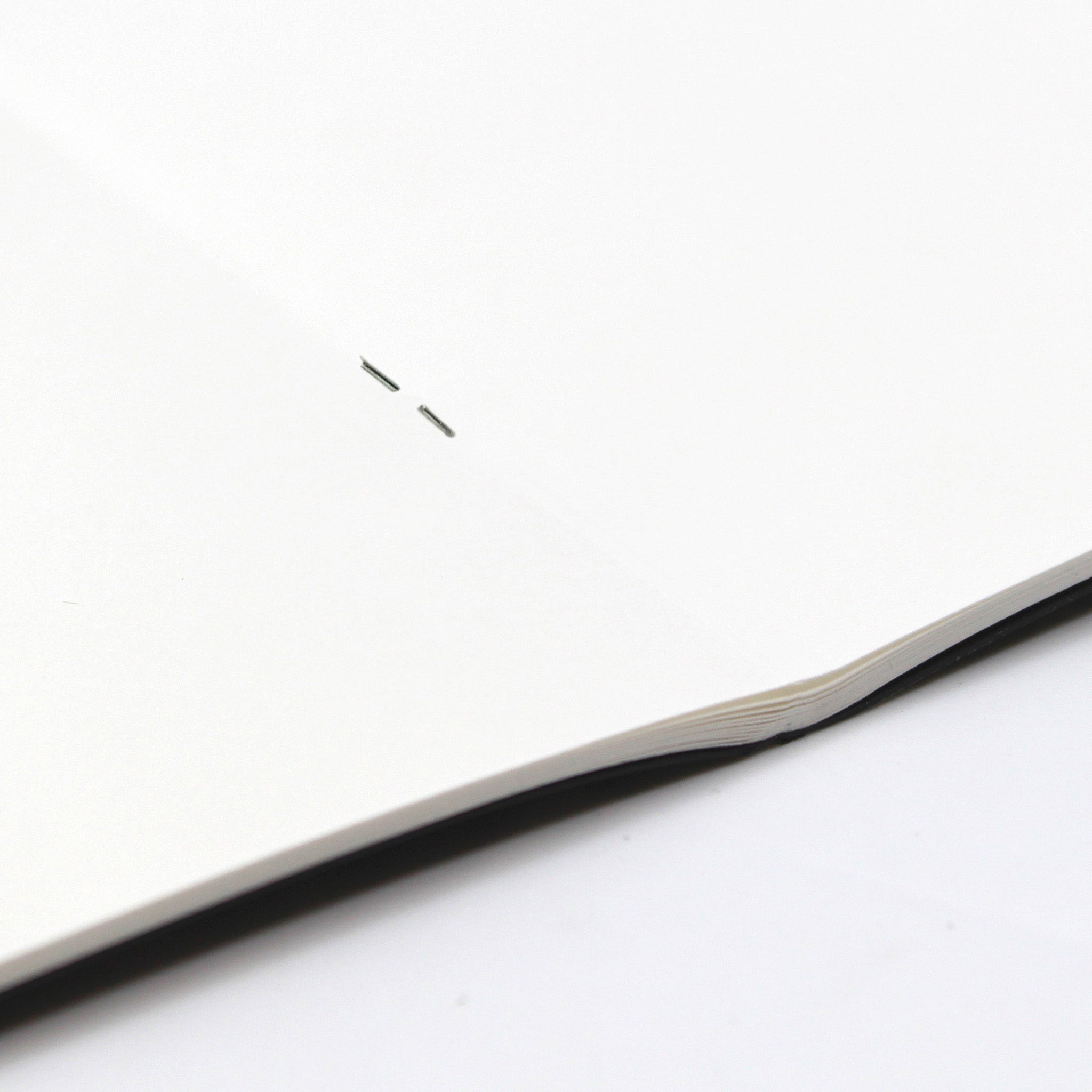 Close Up OF The Staple Binding On  A A3 Field Black Sketchbook 140gsm Paper On A White Background