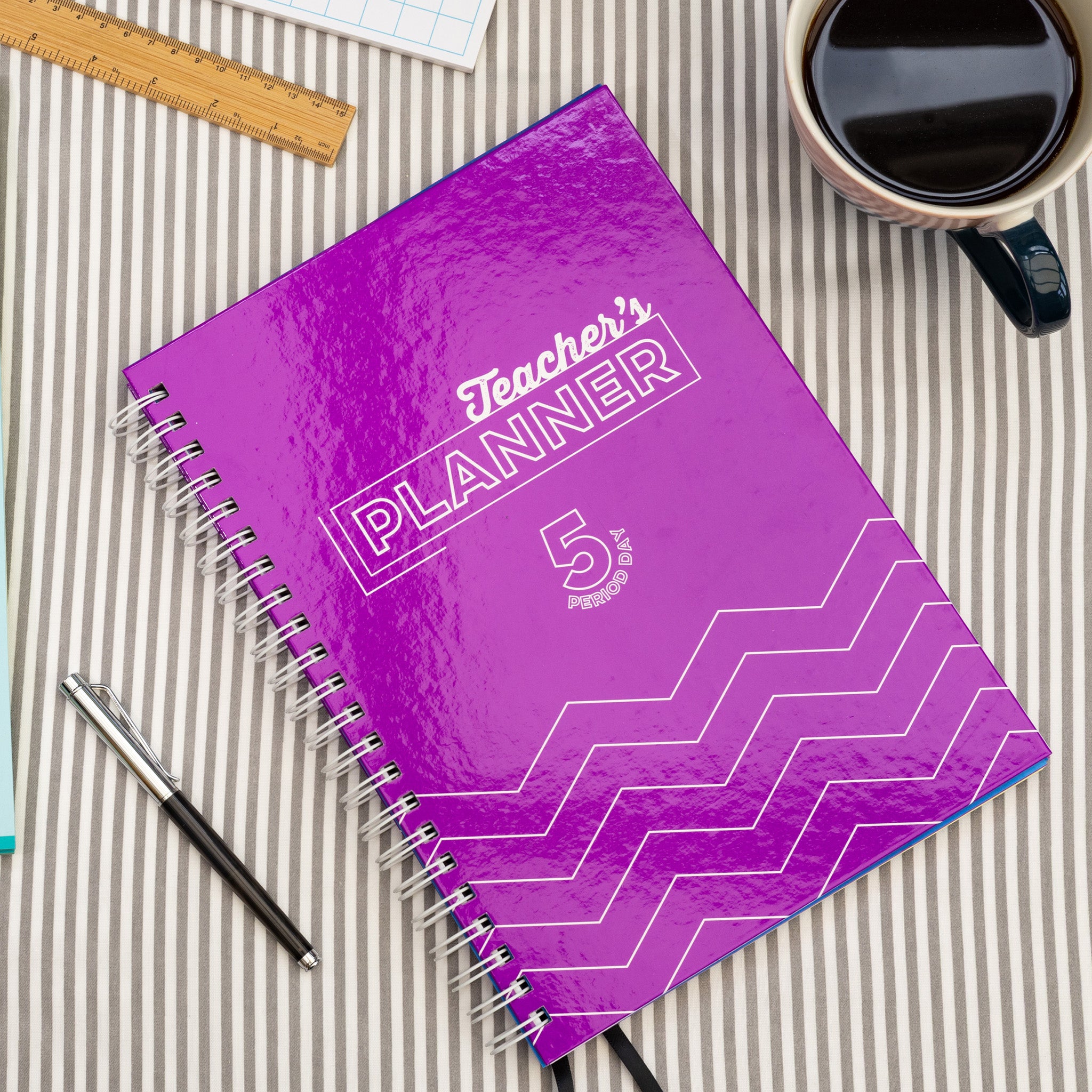 Silvines Purple Teacher's Planner Book On A Striped Table Cloth With A Pen & Coffee Cup.