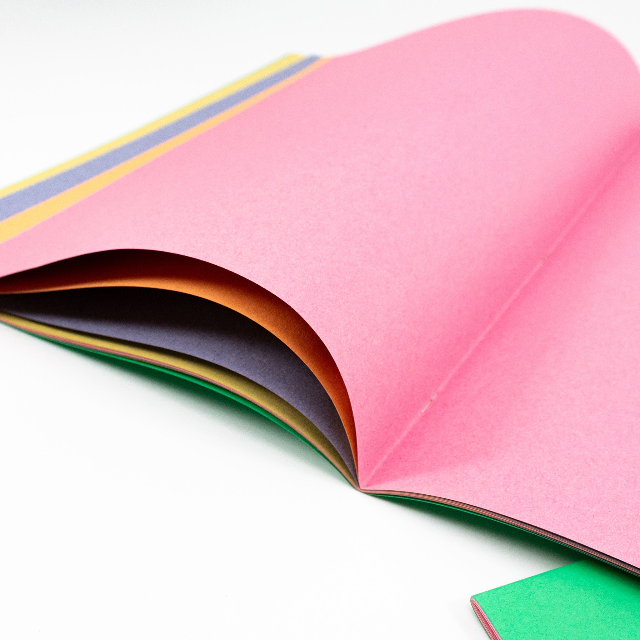 Close-Up Of A Open Pastel Sugar Paper Scrapbook Displaying The Shades Green, Yellow, Pink, & Grey On A White Background