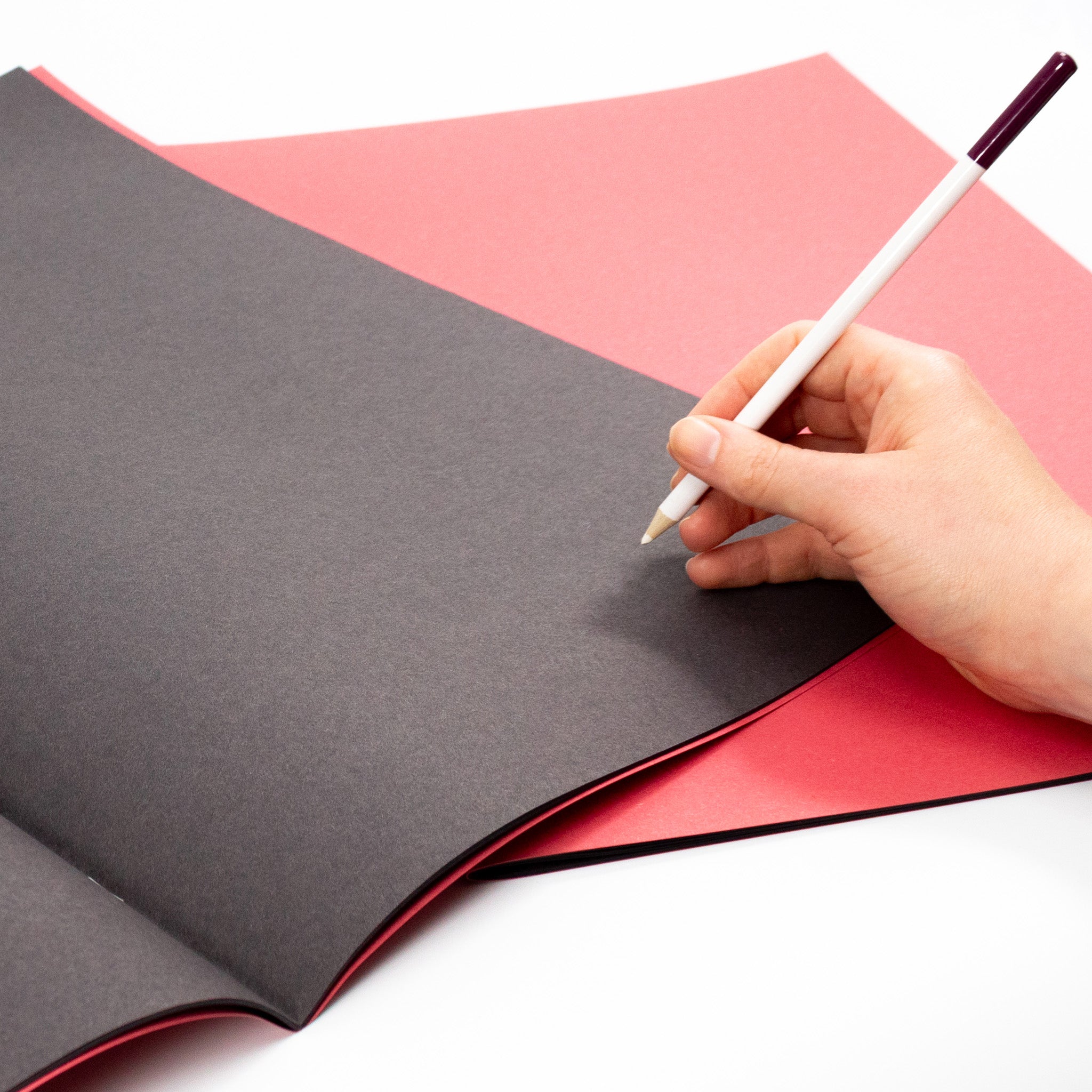 A Hand Holding A White Pencil About To Draw In A Silvine Red Cover Black Sugar Paper Scrapbook For Classrooms On A White Background