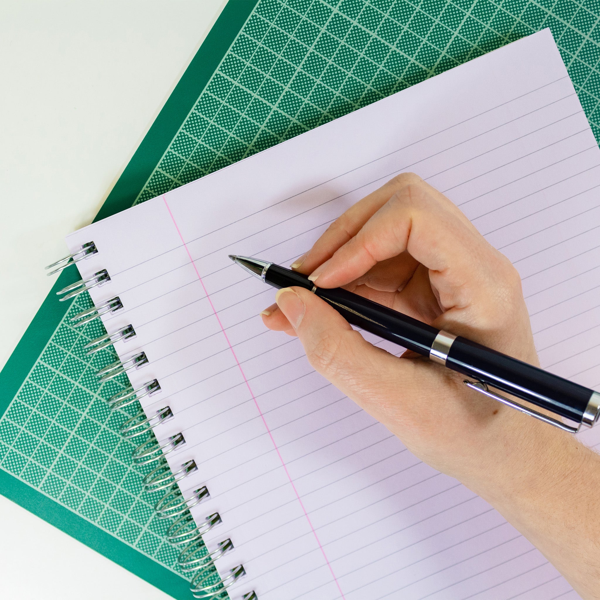 Silvine Project Notebook With 5 Tinted Paper Sections Open On Lilac Page With A Hand About To Pen Some Notes On To It, Laid On A Cutting Mat On A White Background